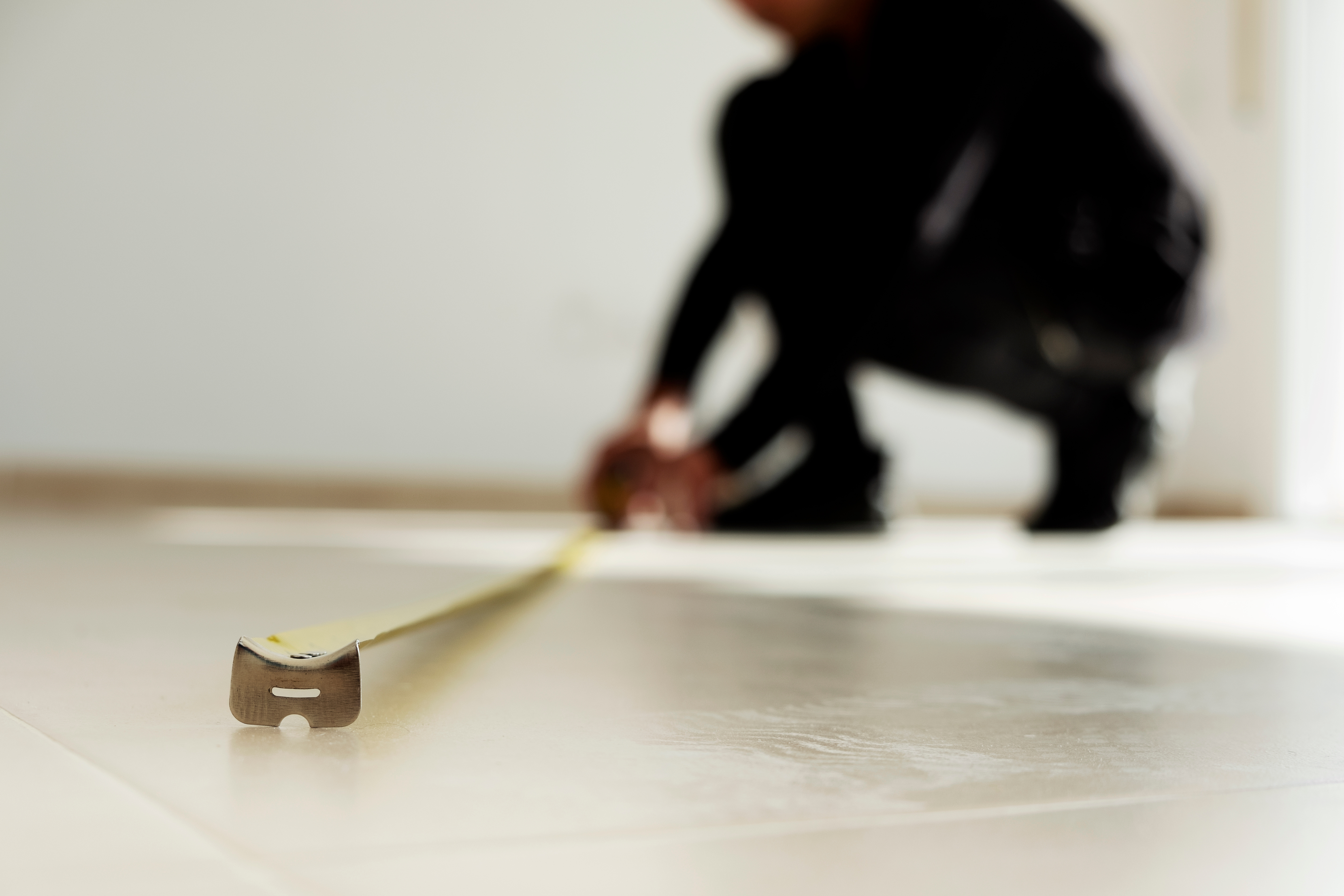 A professional stone care technician using a high-precision measuring tool on a kitchen floor during an estimate visit.