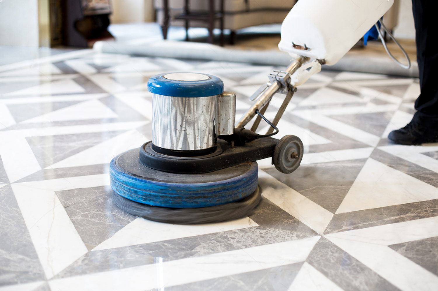 An expert technician operating a planetary floor polishing machine on a large travertine lobby floor.